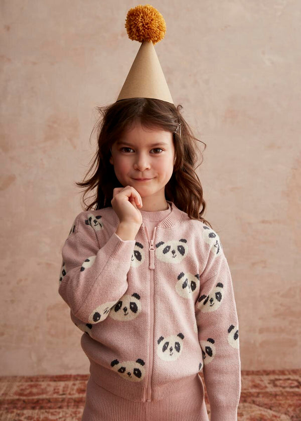 Child wearing a pink hoodie with panda patterns and a beige party hat with a yellow pom-pom on a beige background.