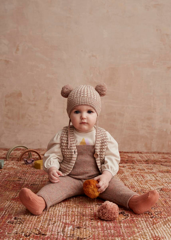 Baby sitting on a textured rug wearing a knitted hat and outfit.