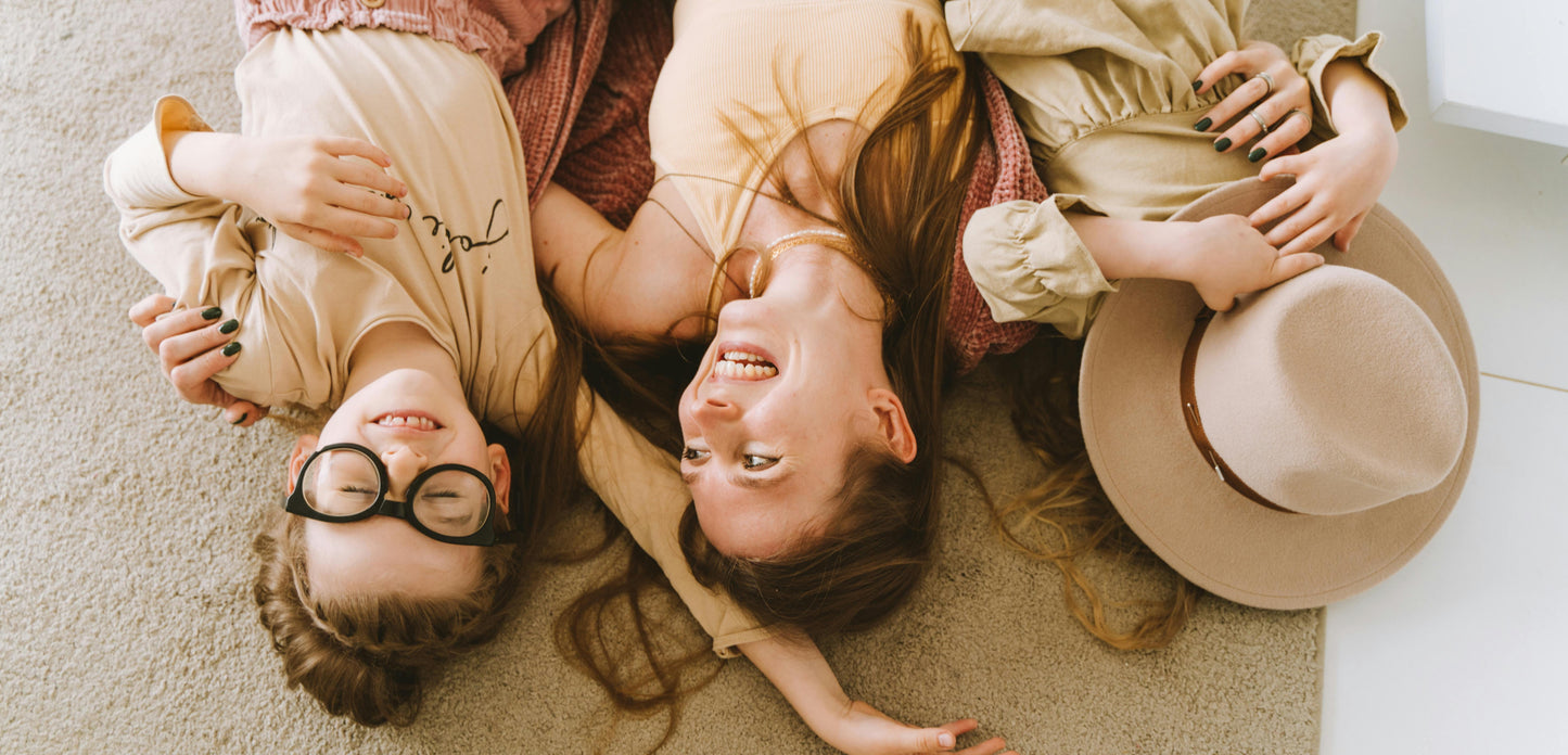Two people lying on a carpeted floor with a hat and glasses.